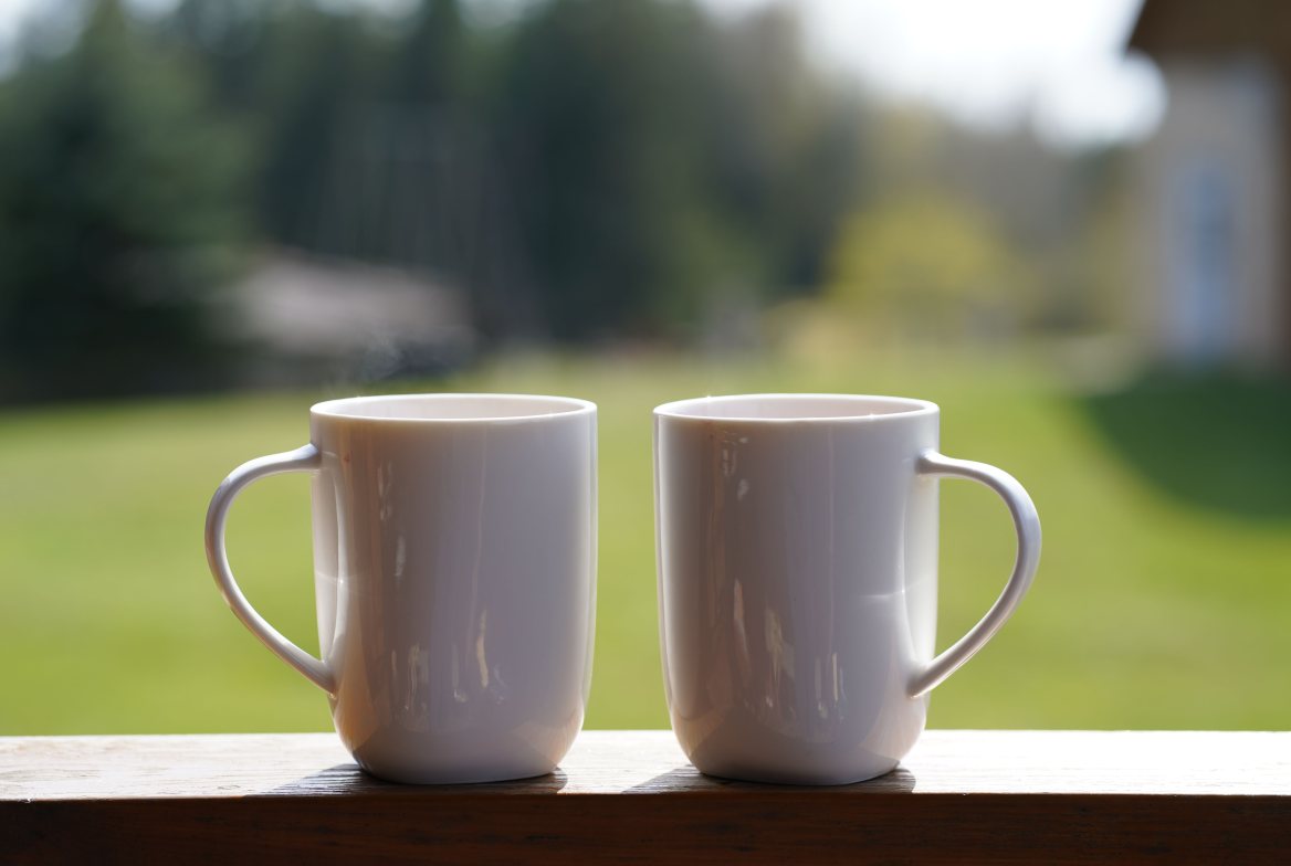 Two white mugs on a porch rail, a sunny lawn beyond