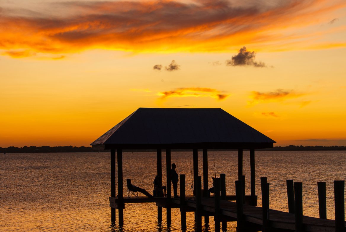 A covered dock silhouetted against an orange sunset over the water