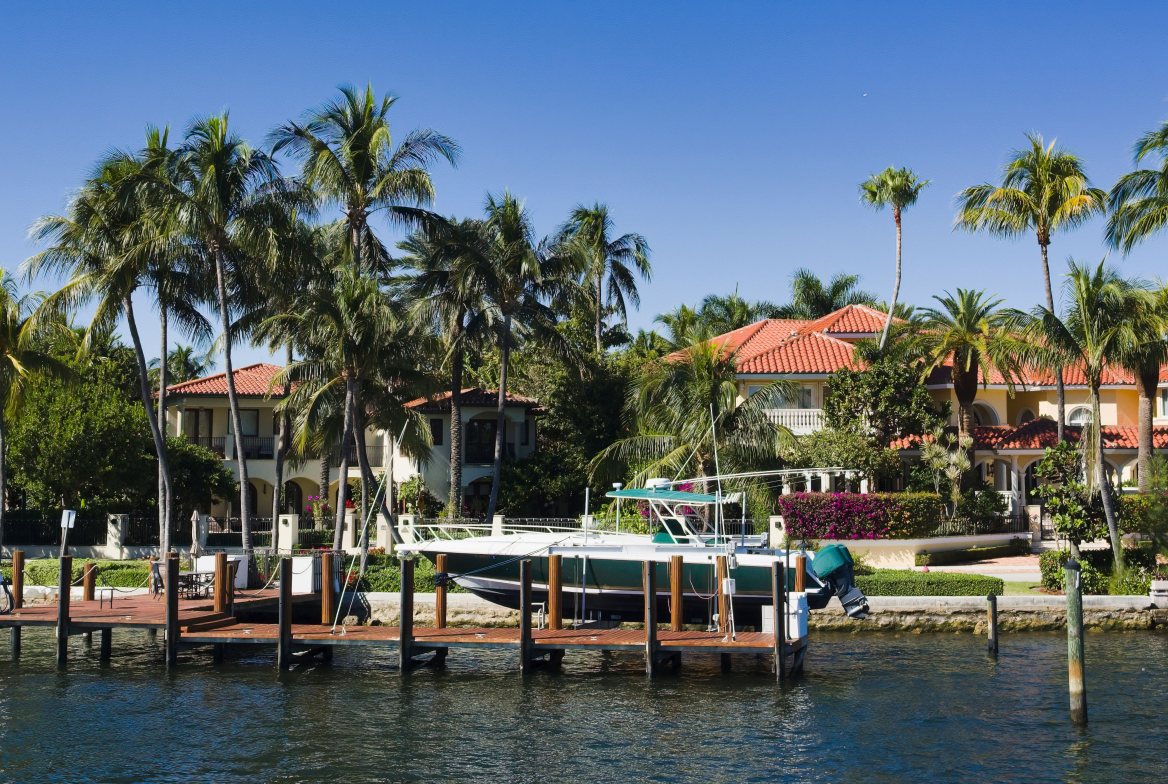 A boat at a private dock on a canal, palms and tile-roofed homes behind