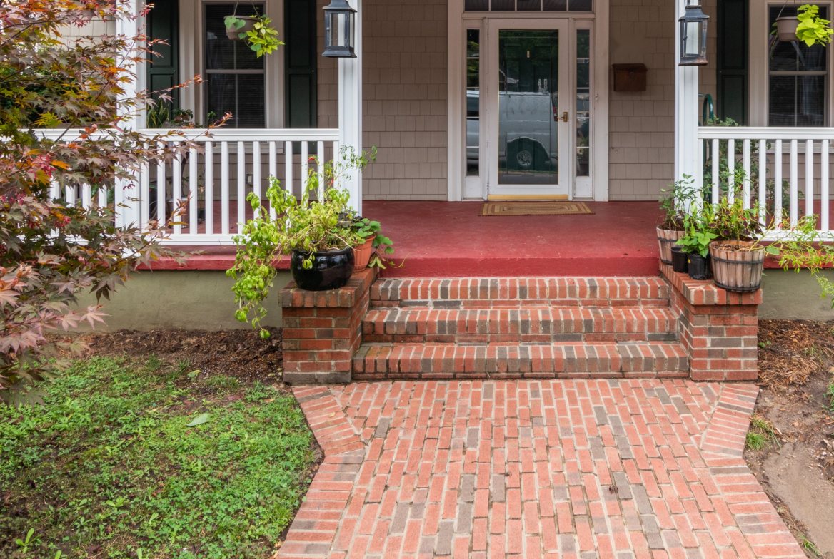 A brick walk and steps up to a white-railed bungalow porch