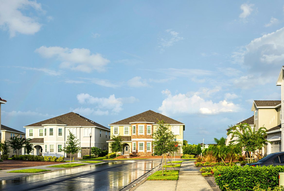 Two-story stucco homes along a rain-wet suburban street under a blue sky