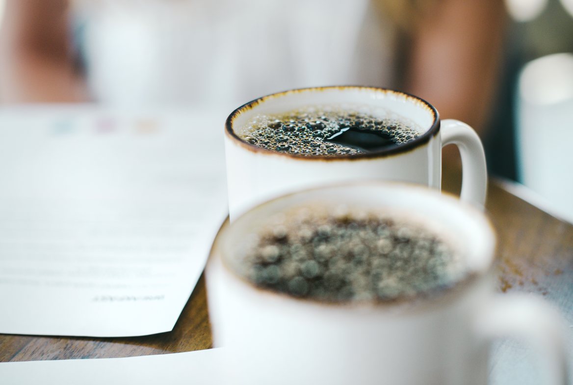Two cups of coffee beside printed pages on a table