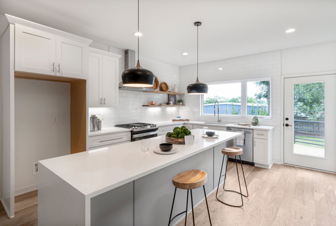 A white kitchen with an island, pendant lights and wood stools