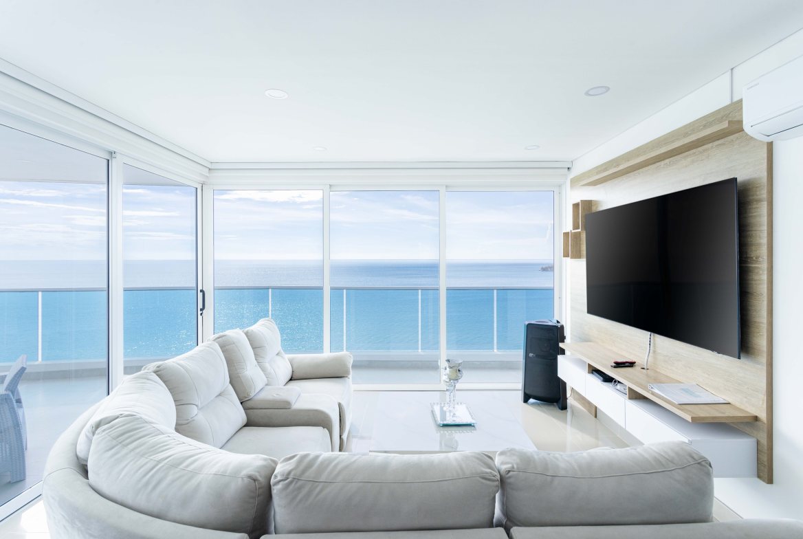 A white living room with a curved sofa facing a glass wall over open water