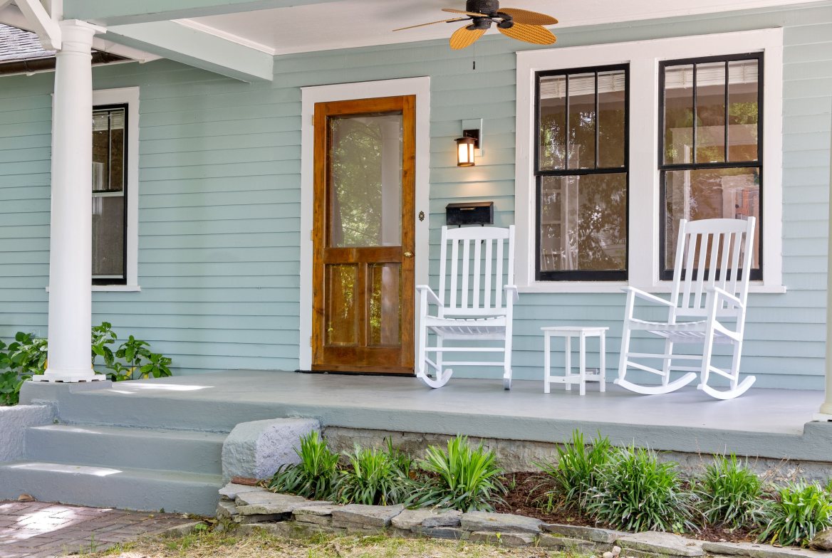 White rocking chairs on a painted bungalow porch beside a wood front door