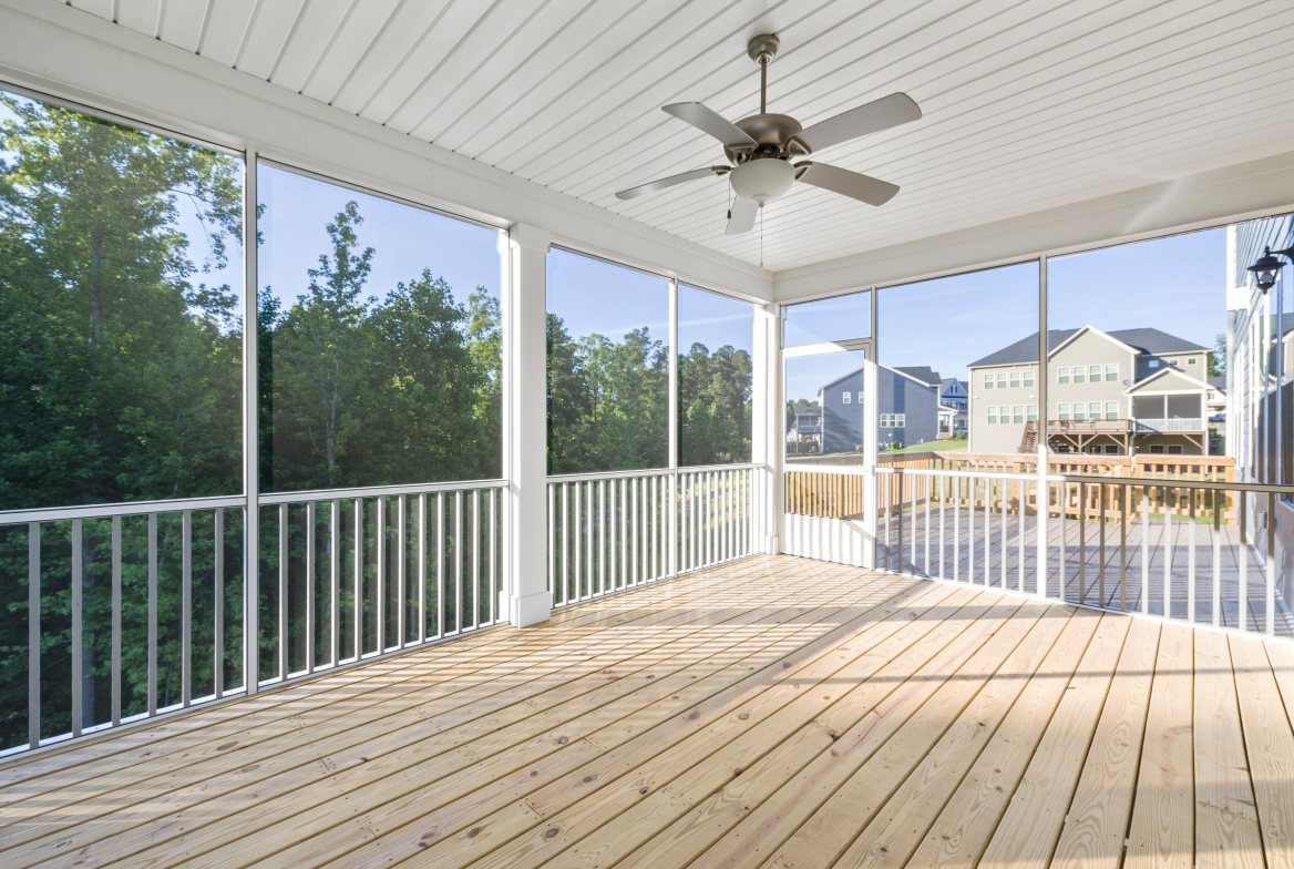 A screened porch with a ceiling fan, looking out to the trees