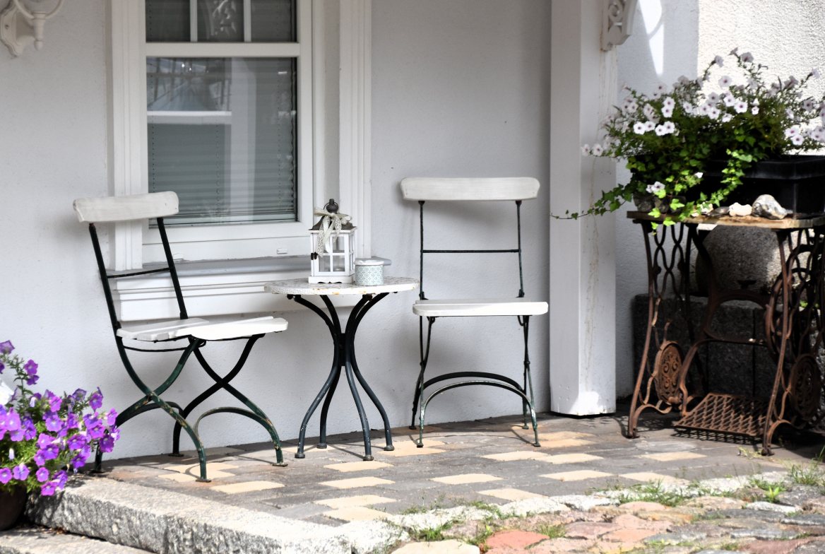 Two bistro chairs on a white porch with petunias by the steps