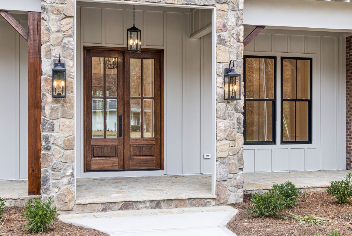 A wood double front door between stone pillars, lanterns lit