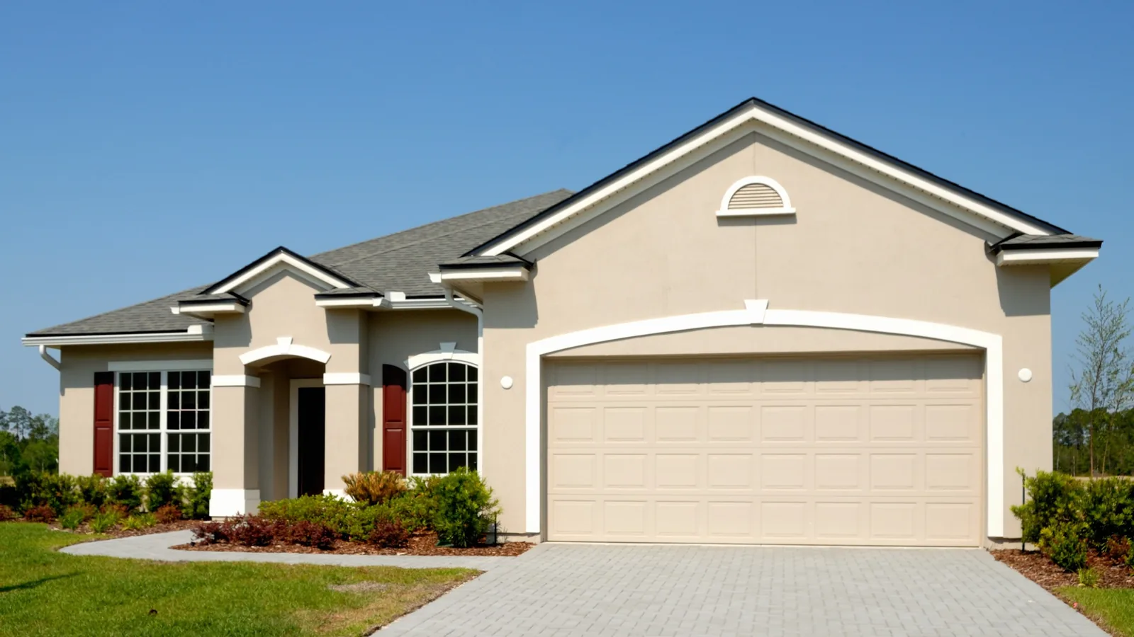 A single-story Florida stucco home with a tile-edged roof, a clipped lawn and a paver driveway under a clear sky