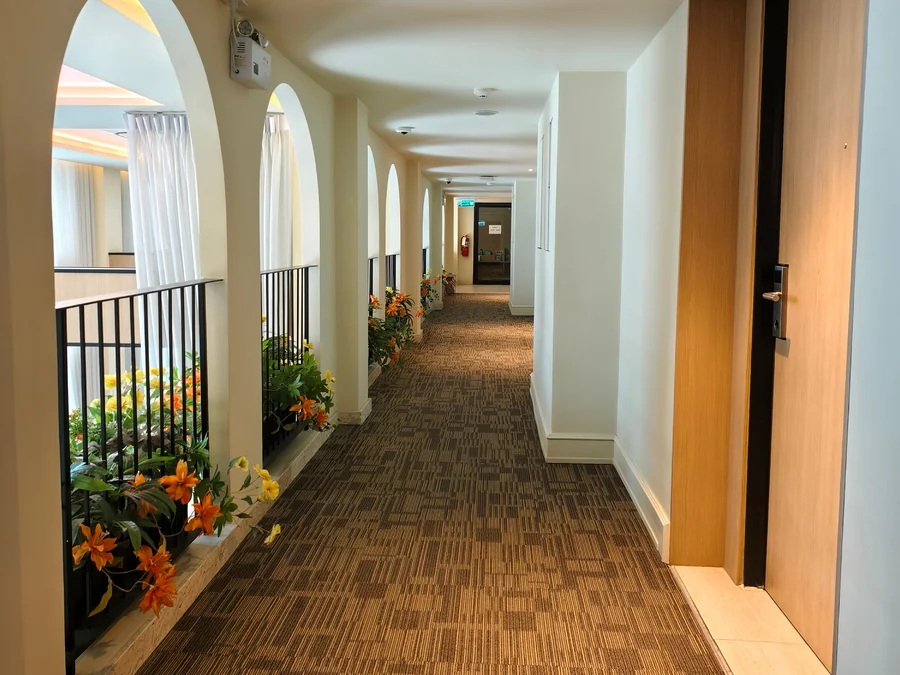 A bright condo hallway with arched openings, potted flowers and a row of unit doors