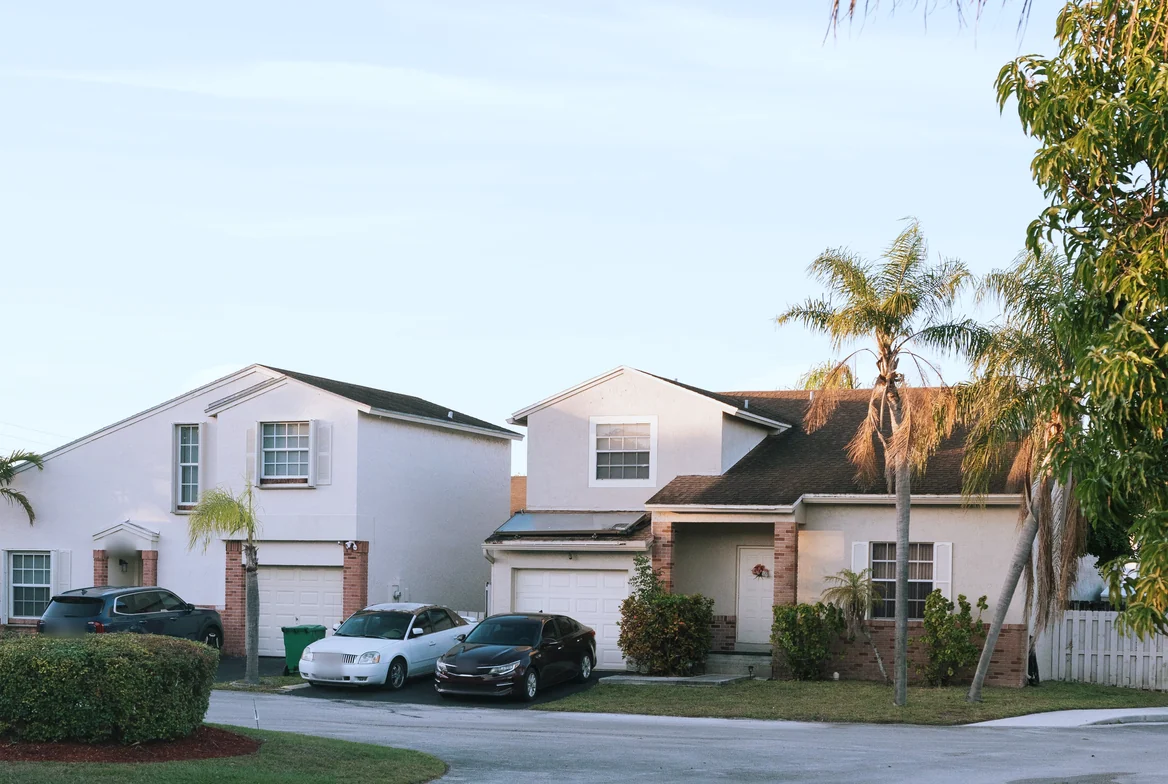 Two stucco houses with palm trees and cars in the driveways on a quiet cul-de-sac