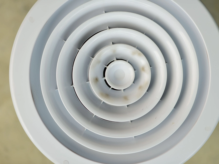 A round ceiling air vent with dust marks around its rings