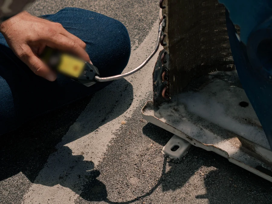 A technician's hand holding a meter lead beside the coil of an outdoor AC unit