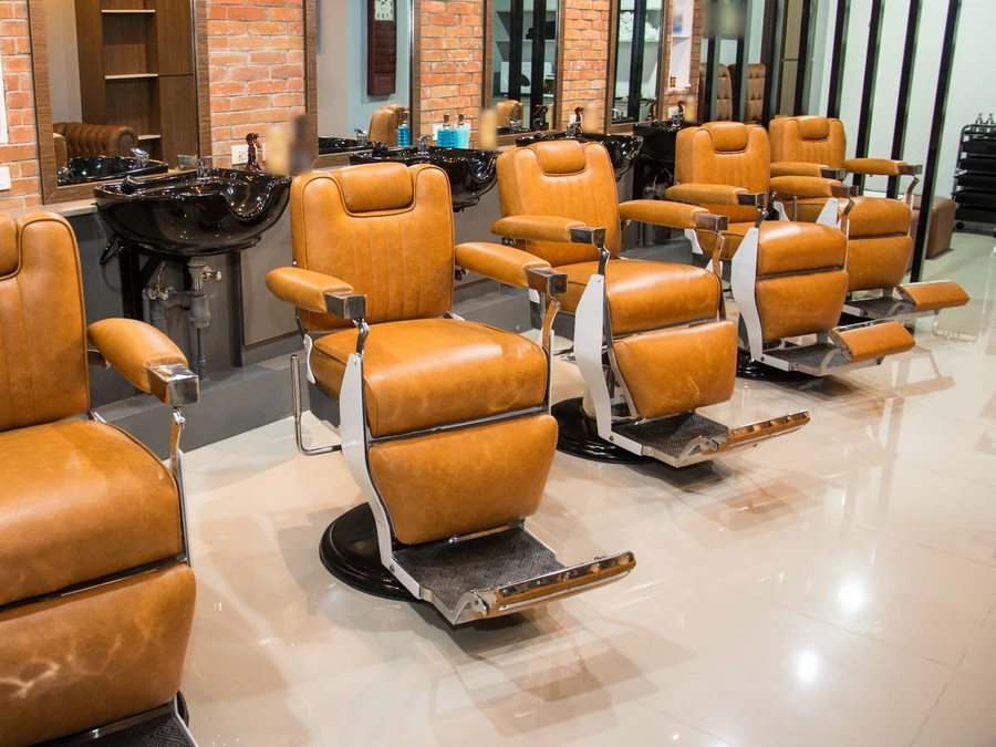 A row of tan leather barber chairs facing the mirrors