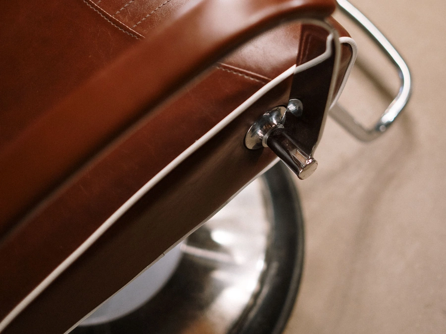 A close-up of a leather barber chair with its chrome lever and base