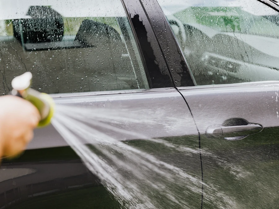 Silver car being rinsed with a hose during a mobile wash