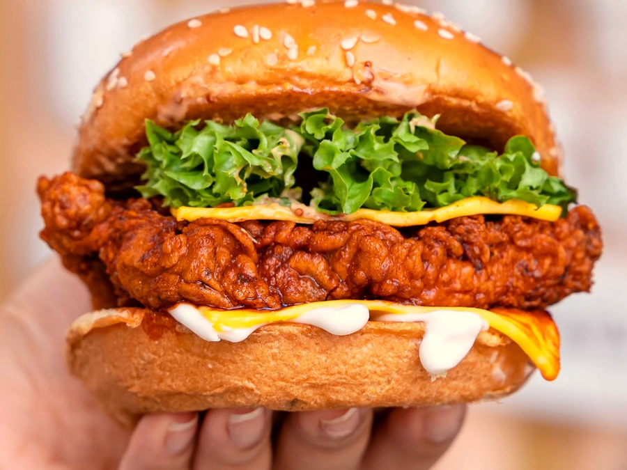 A hand holding a crispy fried chicken sandwich with lettuce and cheese on a brioche bun