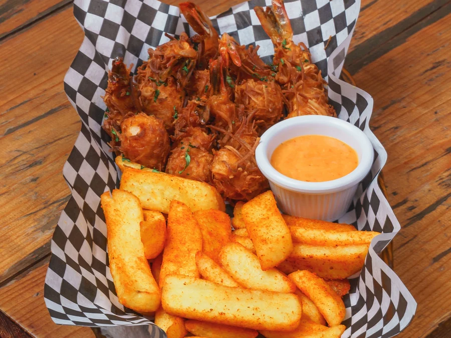 Fried shrimp and fries in a checkered basket with a cup of orange dipping sauce