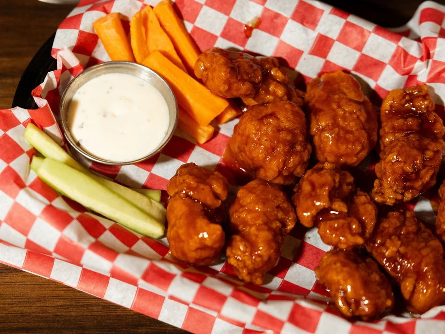 Chicken wings with carrot and celery sticks and a cup of dip, in a basket lined with red checkered paper