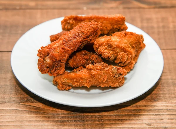 Crispy fried chicken wings piled on a white plate on a wood table