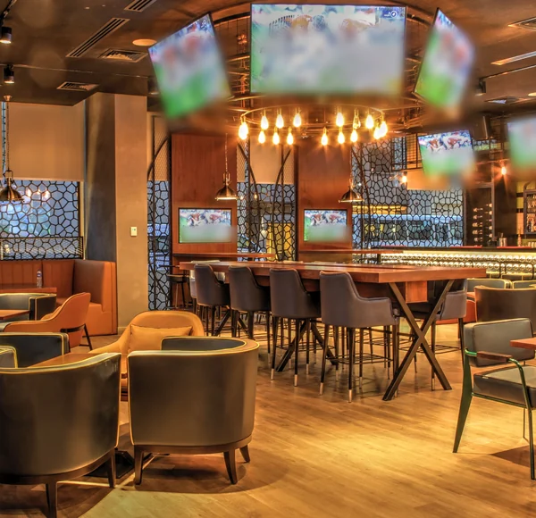 A sports bar dining room with lounge chairs, a long high-top table and TVs along the walls