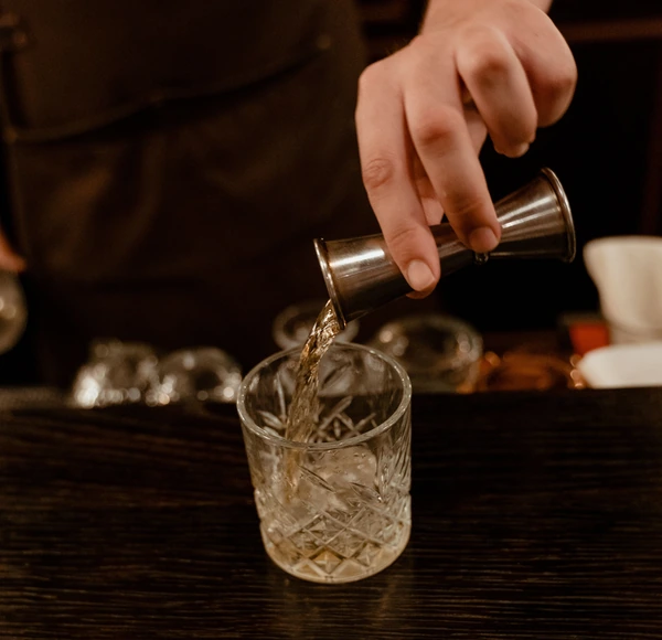 A bartender pouring a drink from a steel jigger into a crystal glass