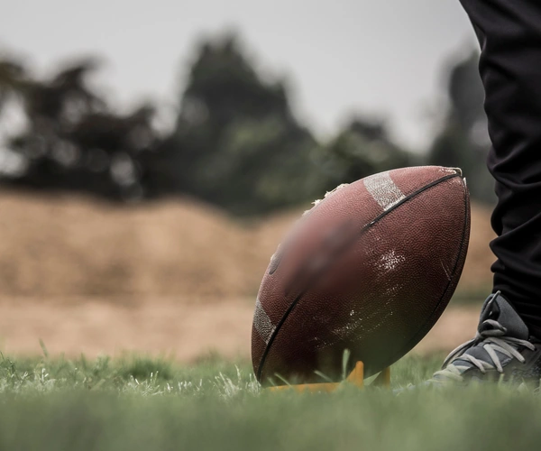 A football resting on the grass beside a player's cleat