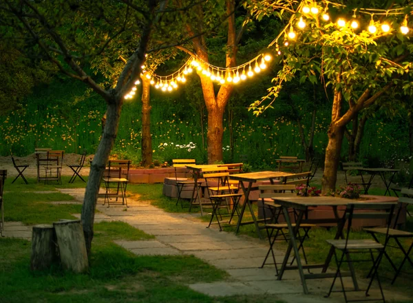 Outdoor tables and chairs under trees strung with lights at dusk