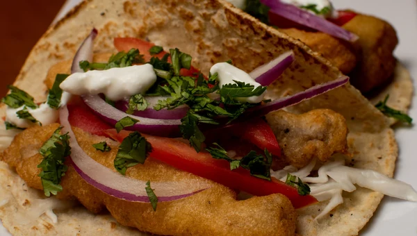 A fish taco with tomato, red onion, cilantro and crema