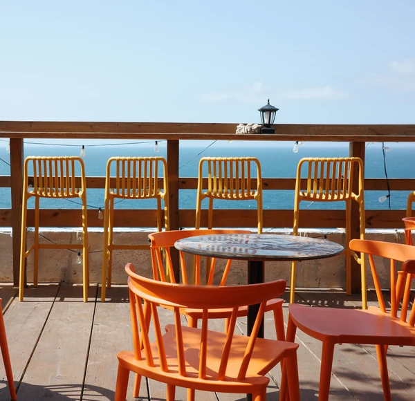 Orange chairs and a round table on a wood deck above open water.